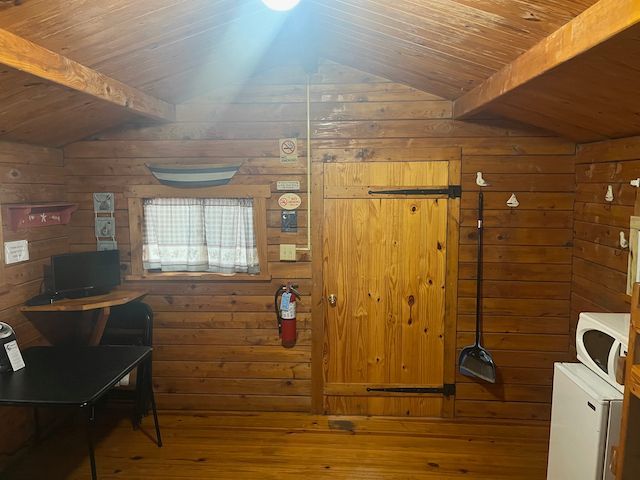 Cozy wooden cabin interior with desk, window, door, and white appliance under a vaulted ceiling