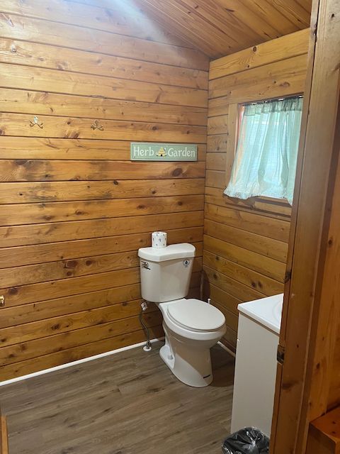 Wood-paneled rustic bathroom with toilet, sink, window, and a small sign on the wall
