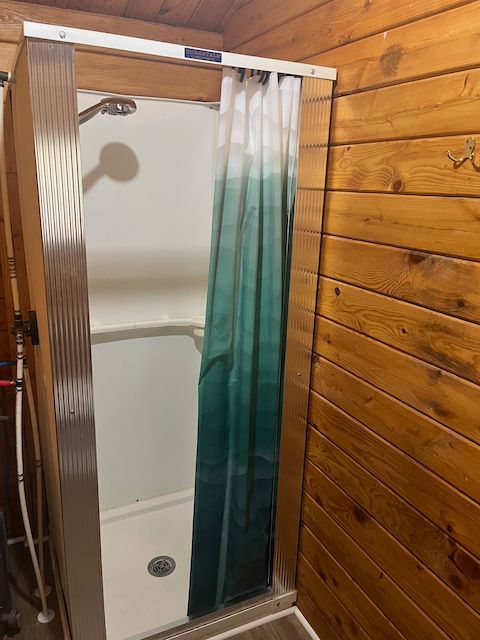 Small shower stall with white walls and teal-striped curtain in a wood-paneled room
