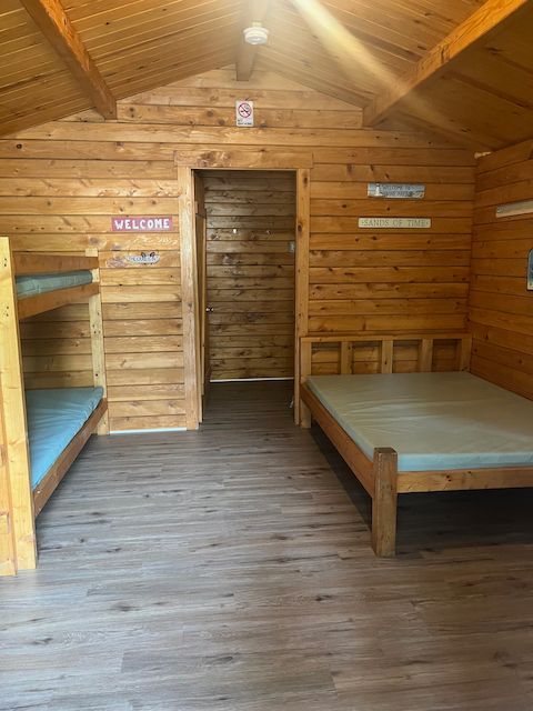 Wooden bunkhouse interior with bunk beds, a single bed, and a central doorway.