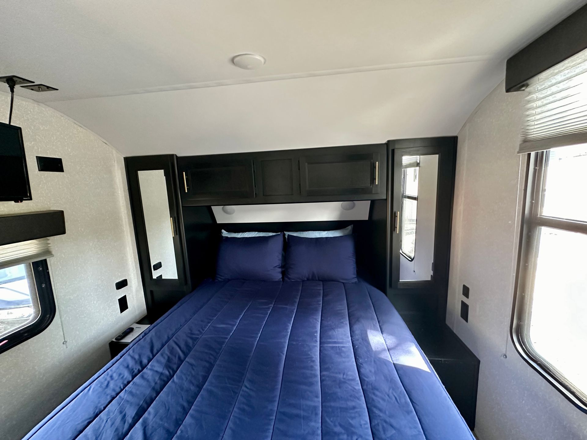 A bedroom in a trailer with a bed and two windows.