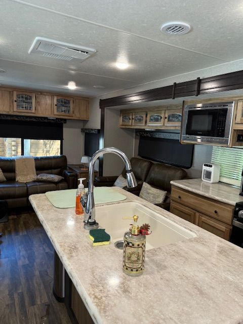 Compact RV kitchen with island, sink, microwave, and couch seating under cabinets and windows