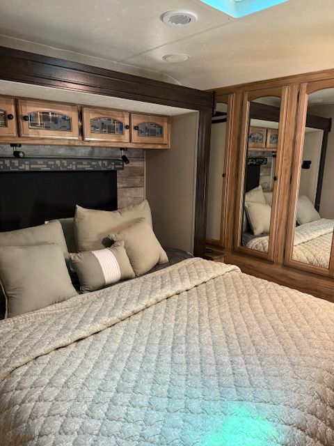 Cozy RV bedroom with quilted bedspread, beige pillows, mirrored wardrobe, and wood cabinets