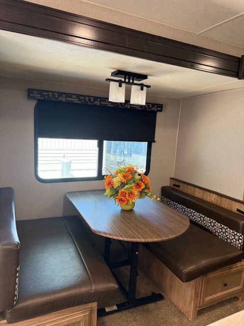 Cozy dining nook with oval table, brown benches, window shades, and a vase of orange flowers.