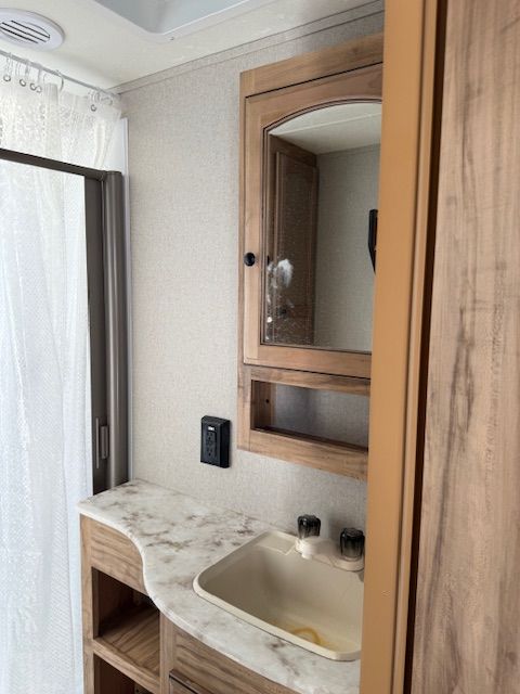 Small bathroom vanity with sink and mirrored cabinet beside a window and shower curtain