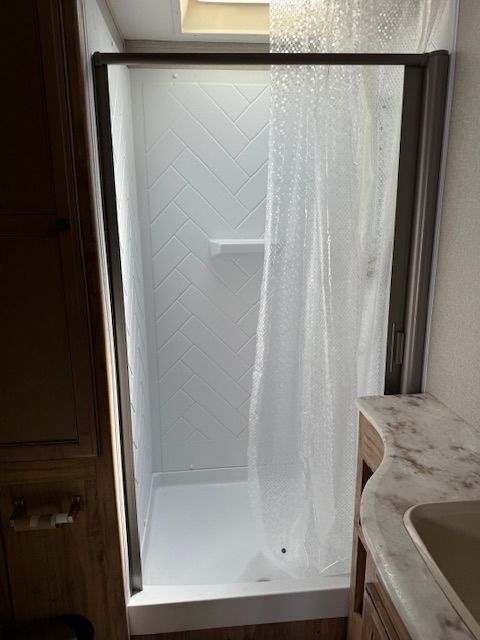 Walk-in shower with frosted glass door, white tile floor, and a marble vanity beside it