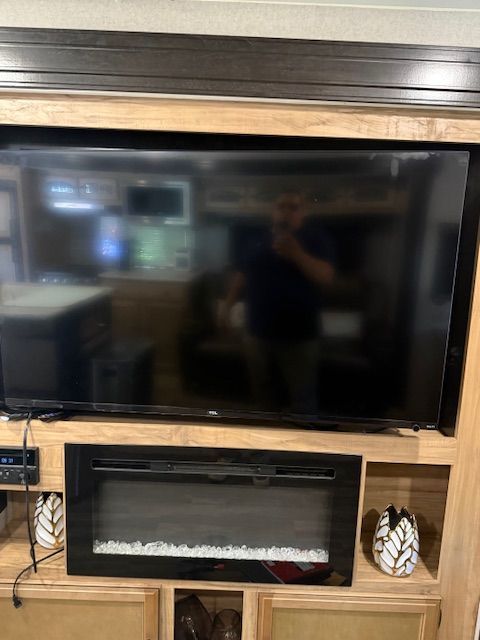 Wall-mounted TV above an electric fireplace with a wooden mantel and decorative accents