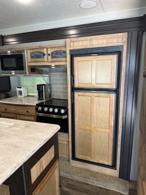 Compact kitchen with wood cabinets, black trim, stove, microwave, and light-tiled backsplash