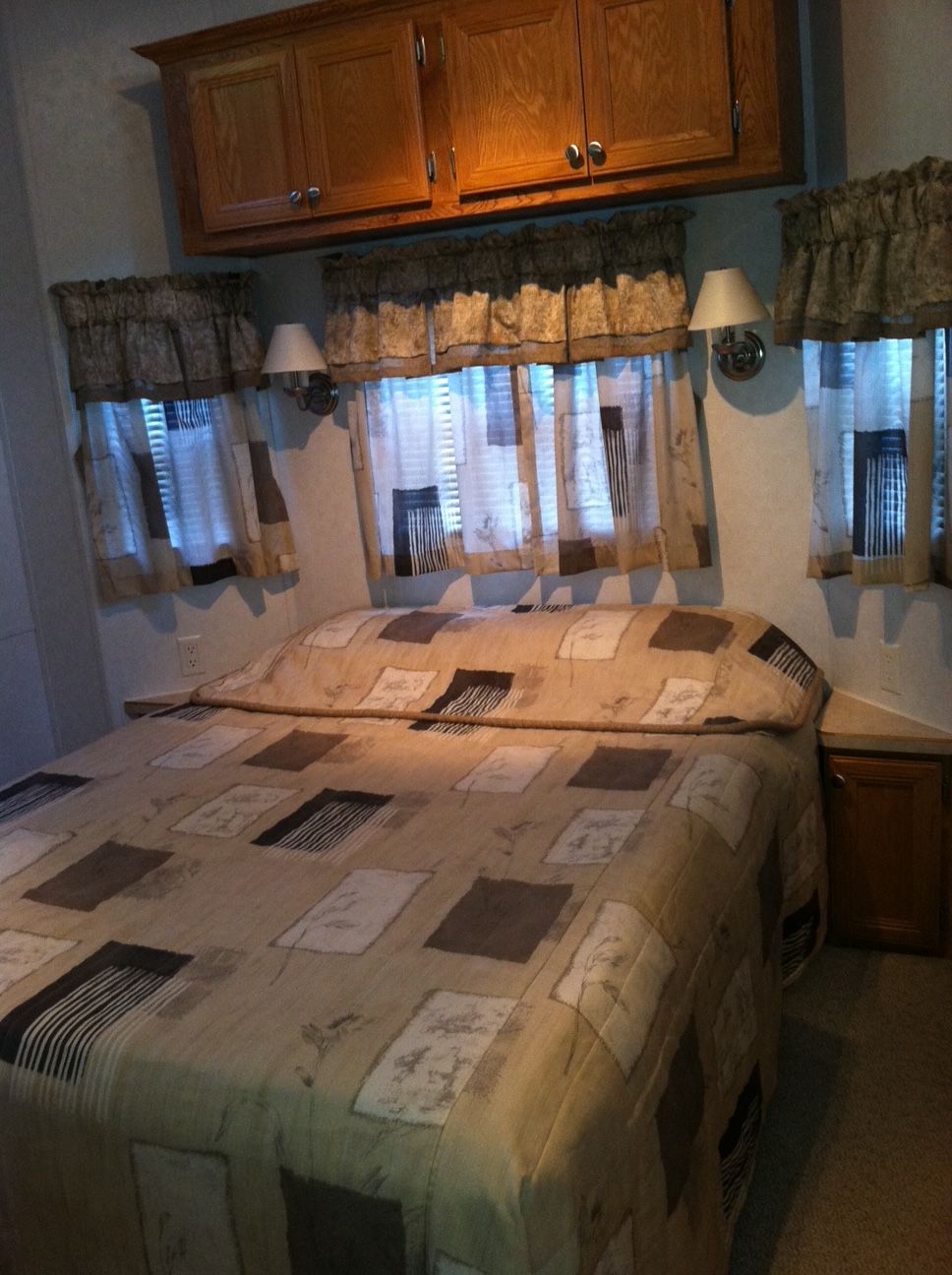 Bedroom with a quilted bedspread, wooden cabinets, and windows with curtains and valances.