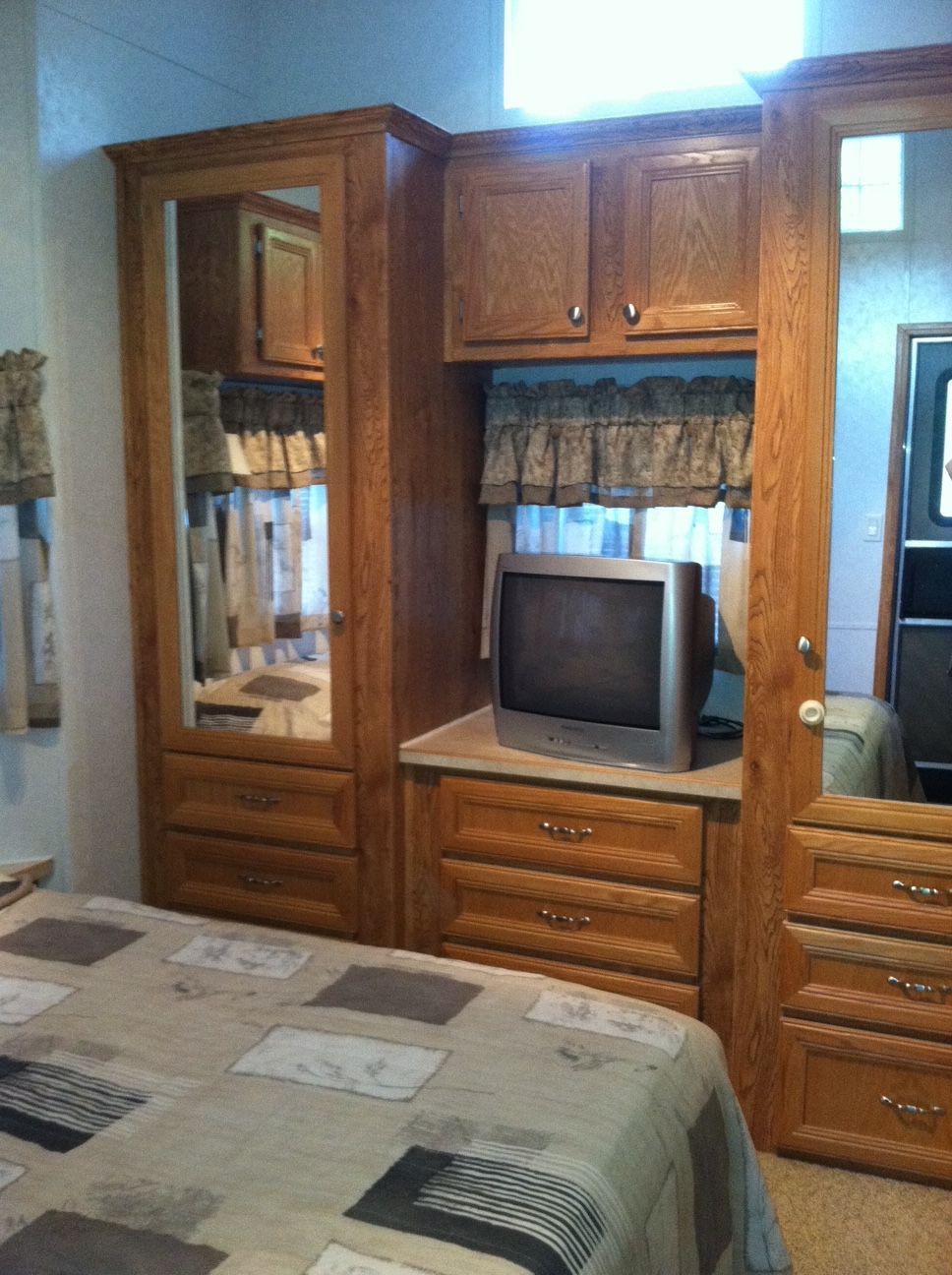 Wood-paneled bedroom with mirrored closet, dresser, TV, and bedspread in the foreground