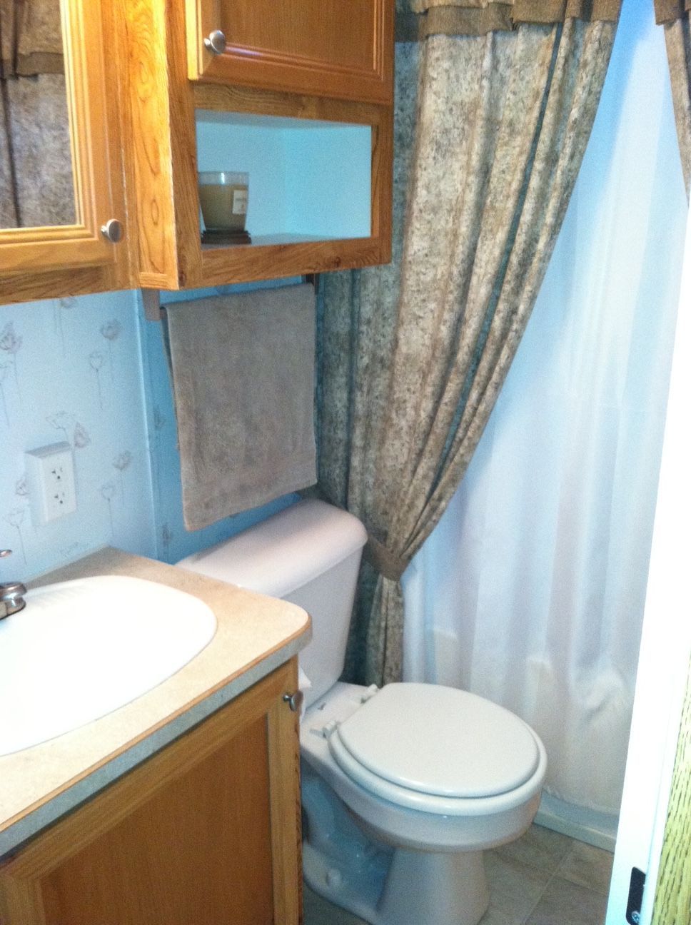 Small bathroom with sink, toilet, wood cabinets, and a blue shower curtain.
