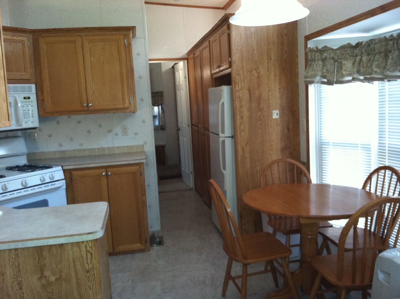 Small kitchen with wood cabinets, white appliances, a round table, and chairs near a window.