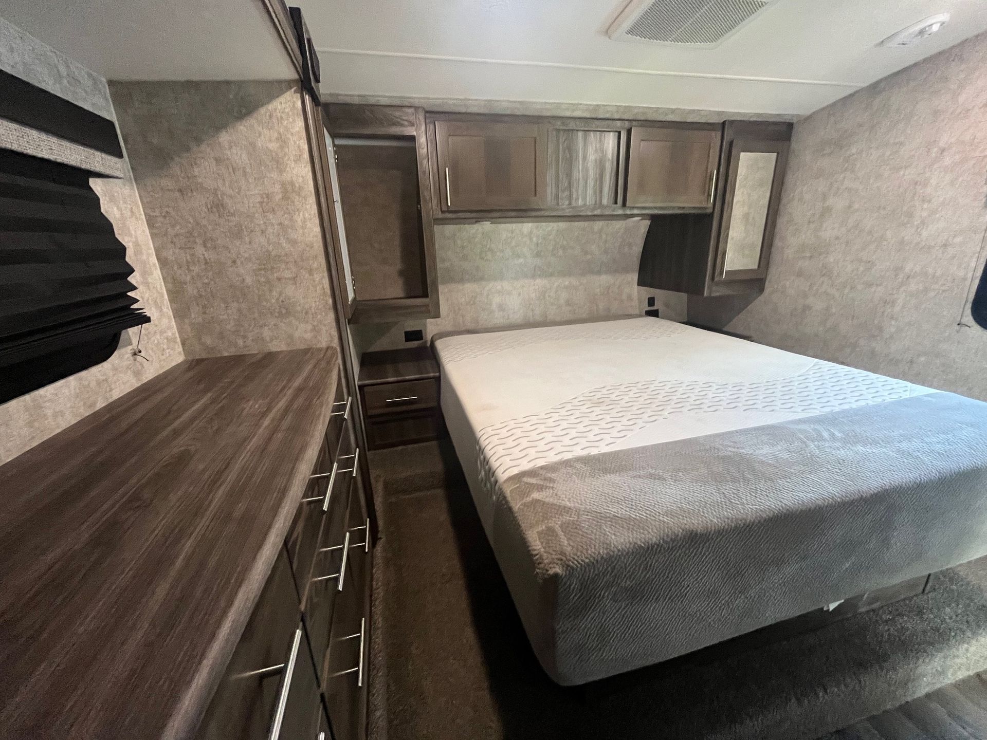 Compact bedroom interior with a bed, built-in cabinets, and wood countertops inside a small camper or RV.