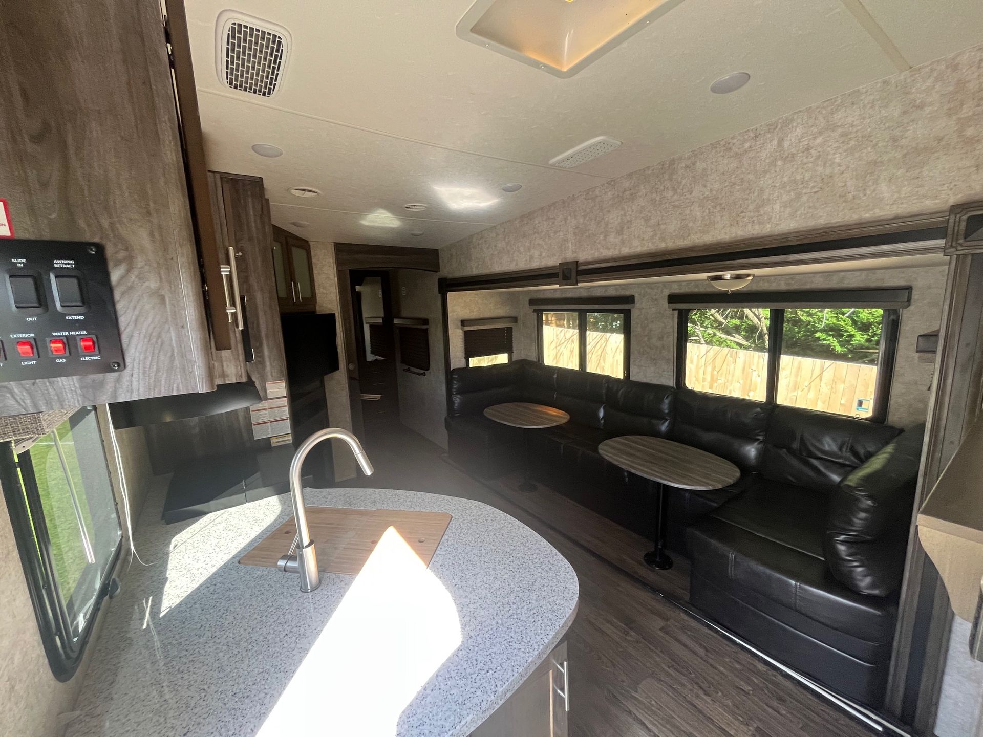 Compact RV kitchen and lounge with gray countertops, sink, black bench seats, and large side windows.