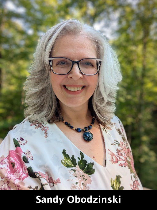 Woman with gray hair and glasses smiles outdoors.