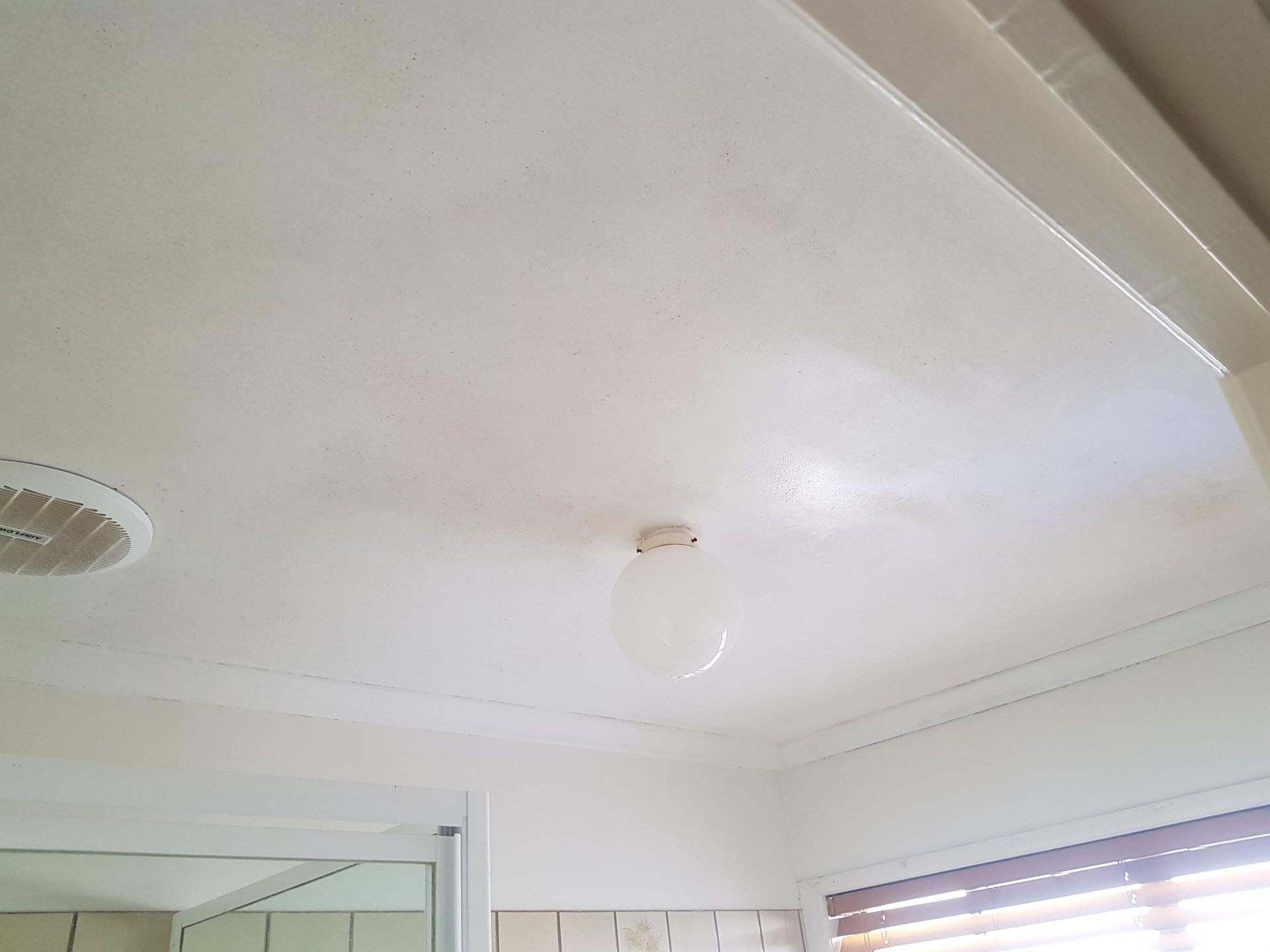 White ceiling with a central light fixture and a vent above a doorway in a room