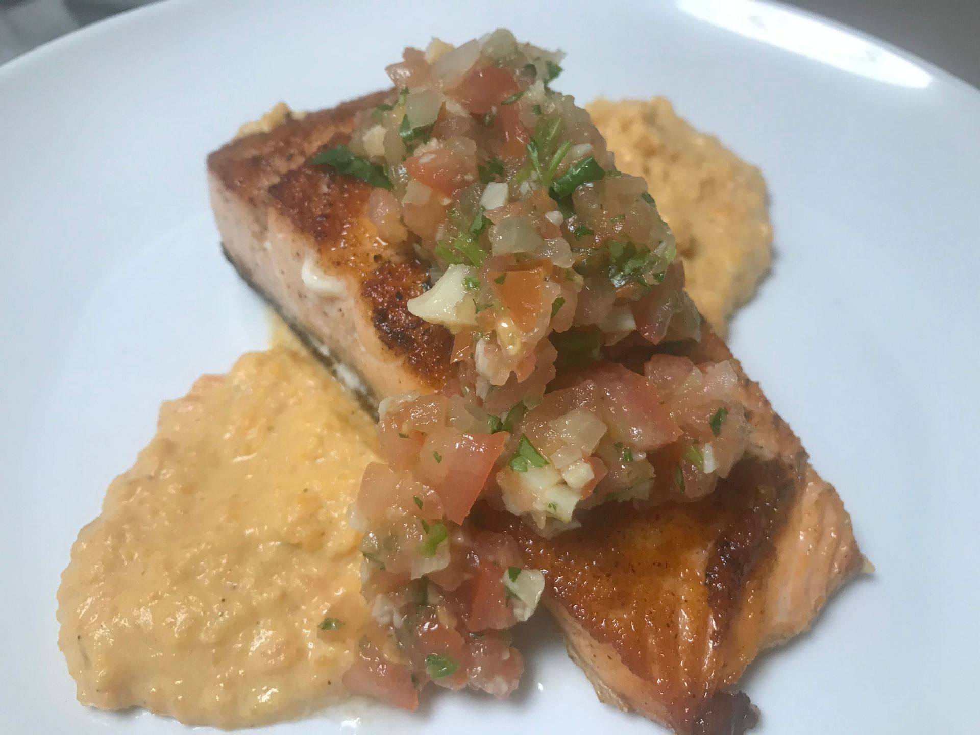 Seared fish topped with salsa, served on a plate with creamy side dishes