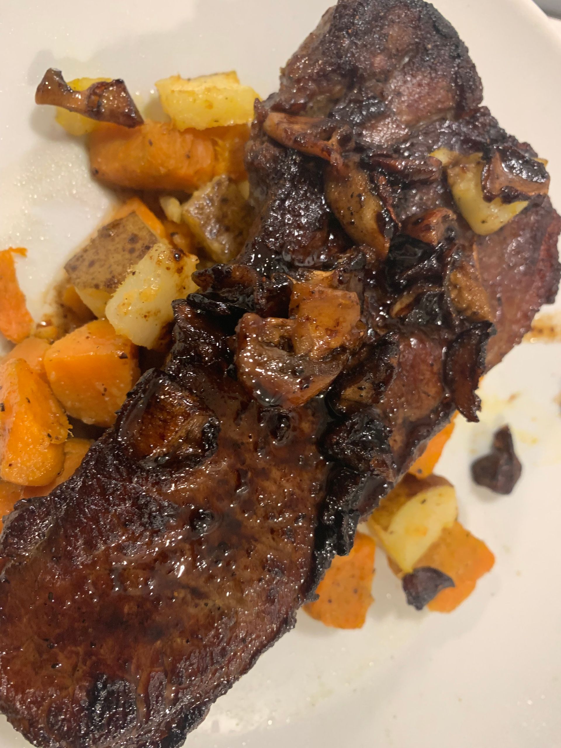 Grilled steak with caramelized onions and diced potatoes on a white plate