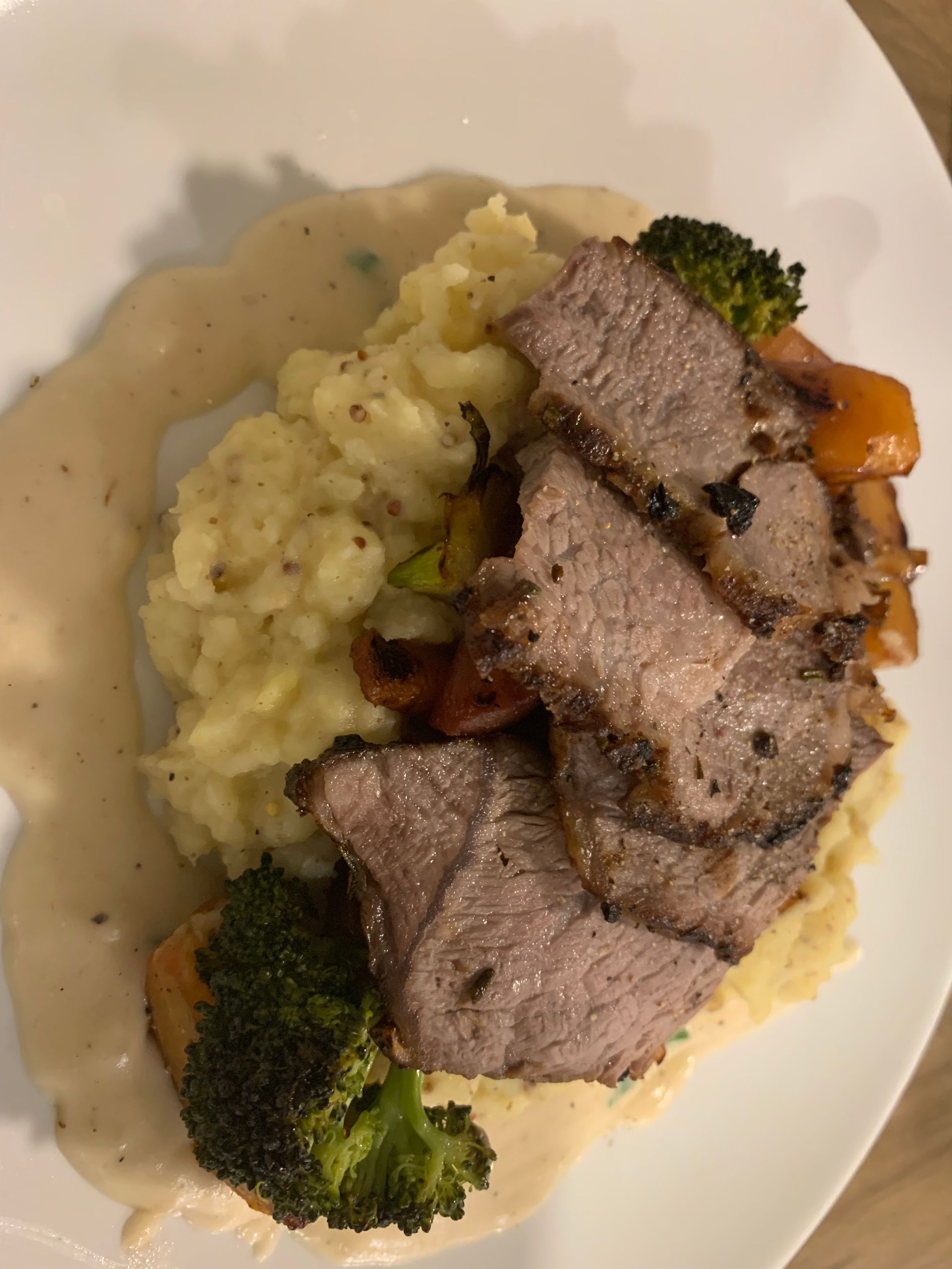 Plated roast beef slices with mashed potatoes, broccoli, and vegetables in cream sauce