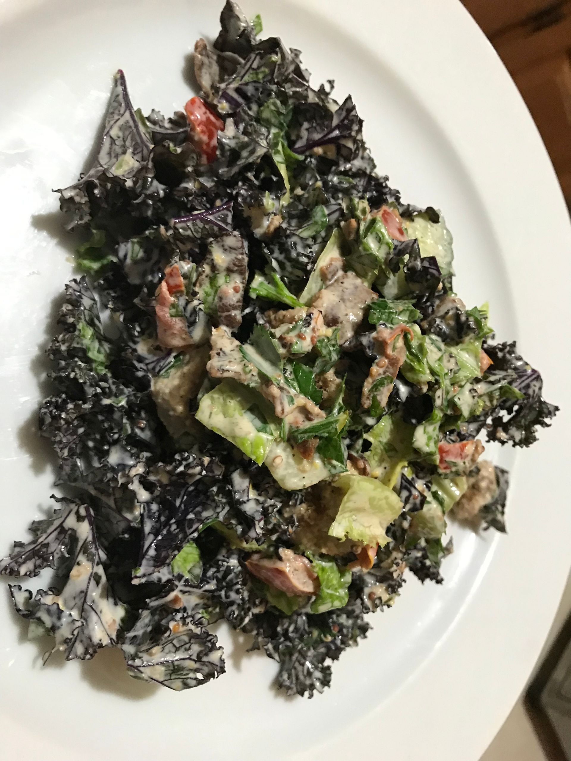 Dark leafy salad on a white plate with green avocado and diced bacon pieces