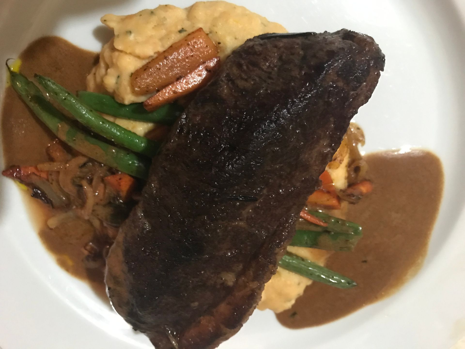 Plated steak with brown gravy, green beans, and mashed potatoes on a white dish
