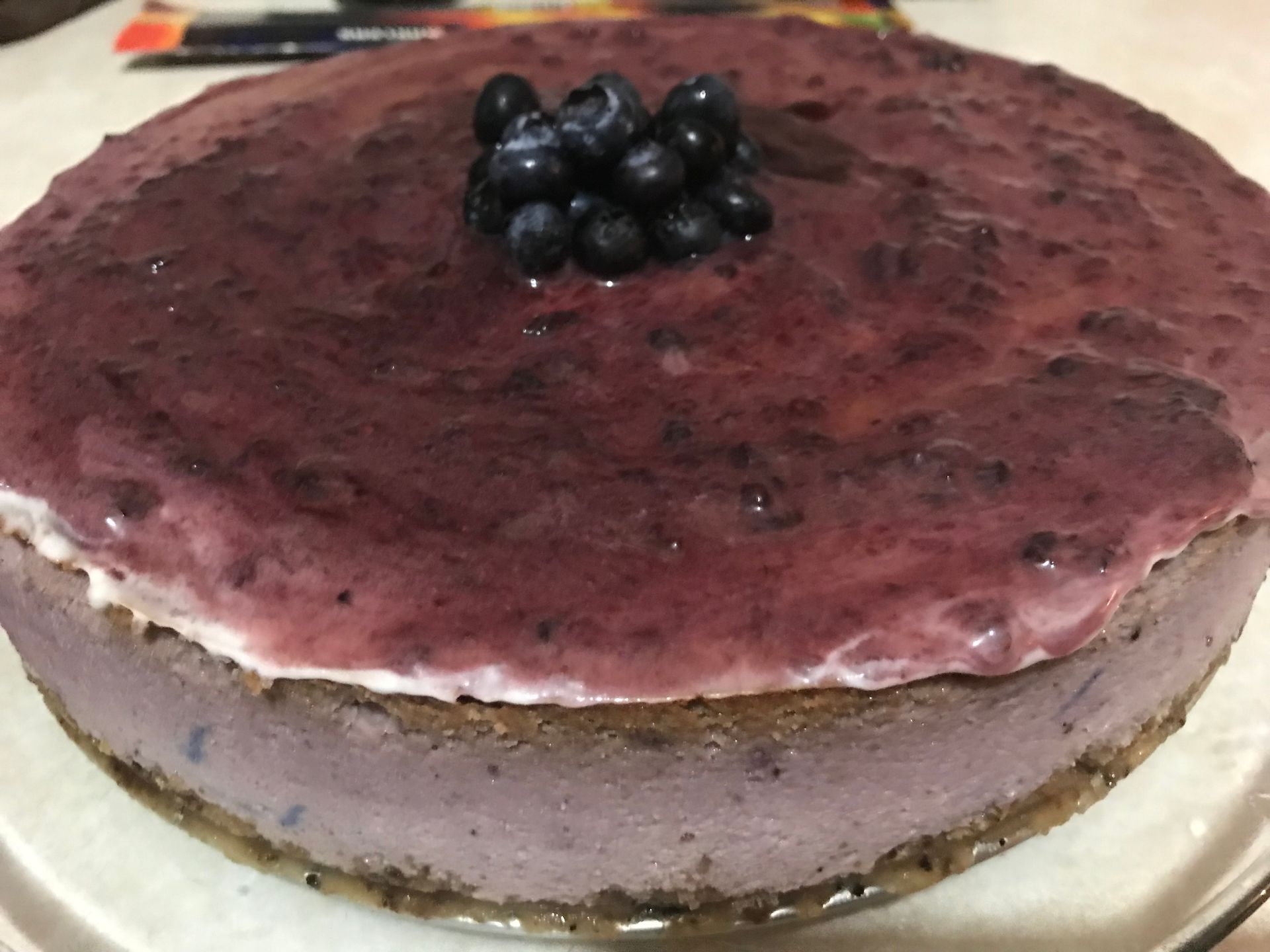 Purple berry cheesecake topped with blueberries on a white plate