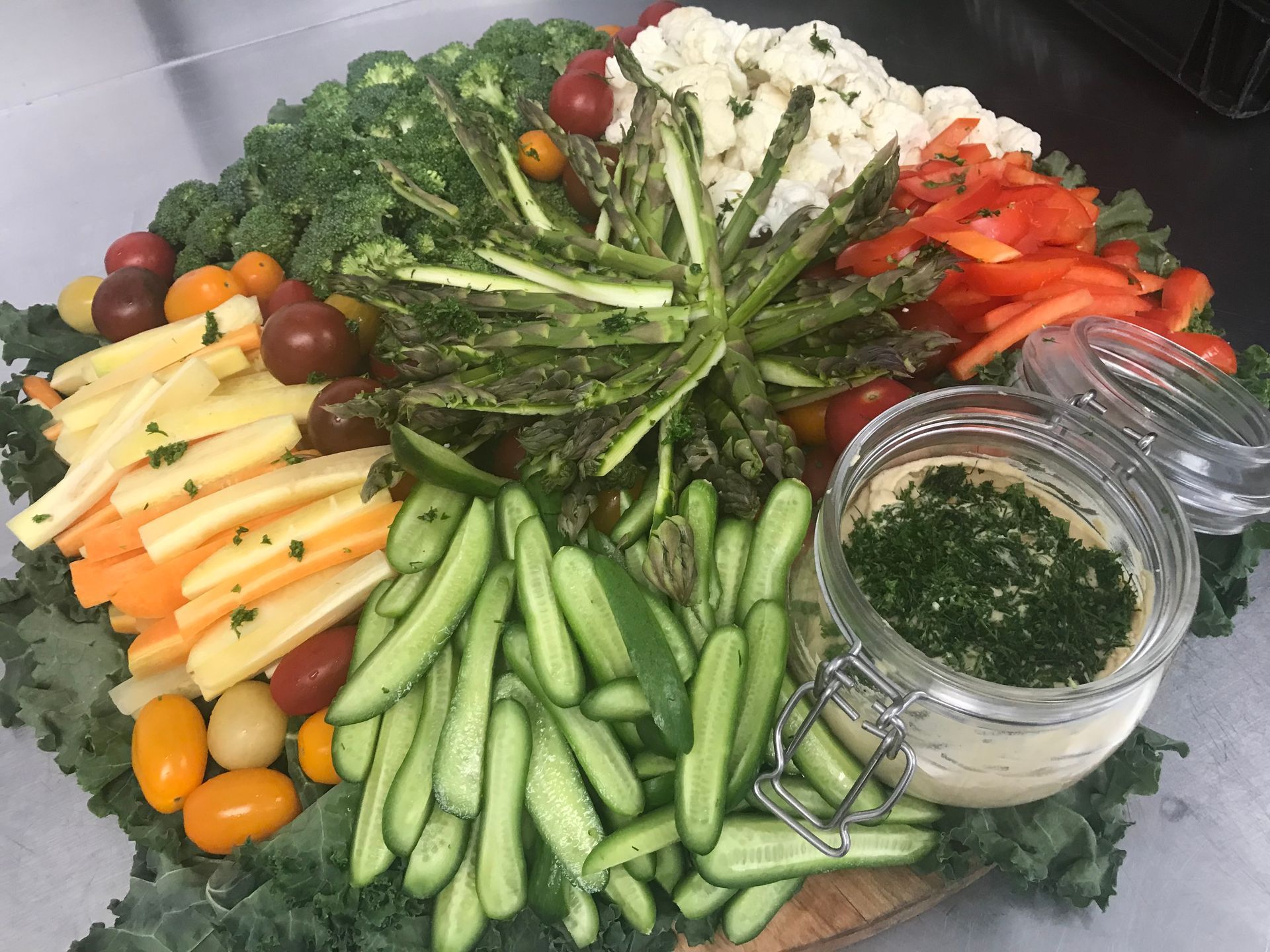 Assorted fresh vegetables arranged in a circular platter with a jar of herb dip in the center
