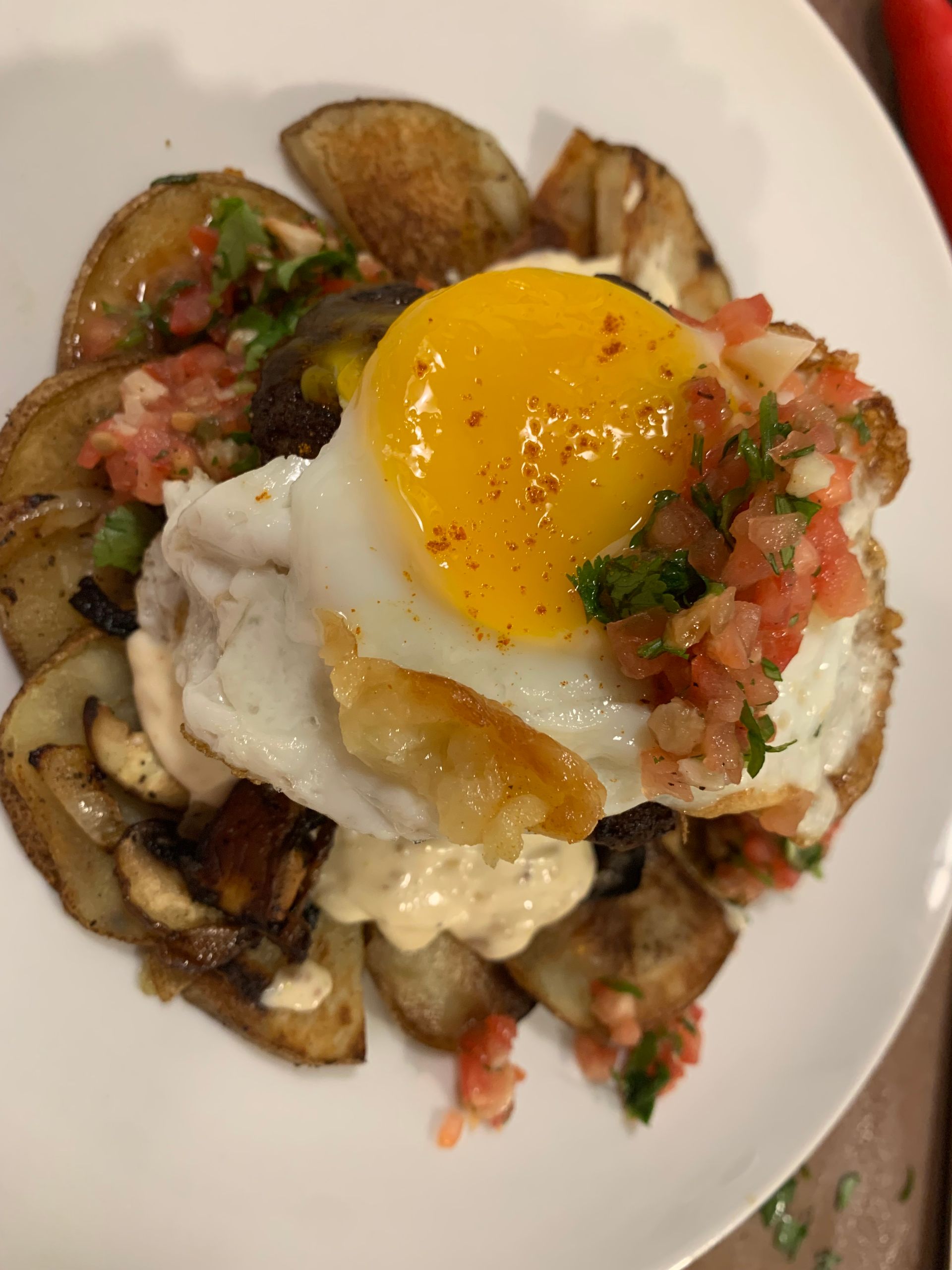 Fried egg over potatoes topped with chopped tomato and herbs on a white plate
