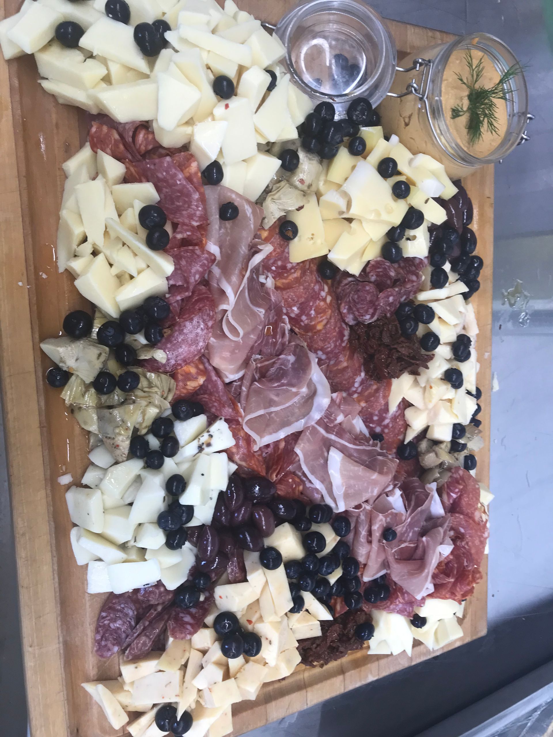 Charcuterie board with cheese cubes, salami, grapes, crackers, and two small dip cups