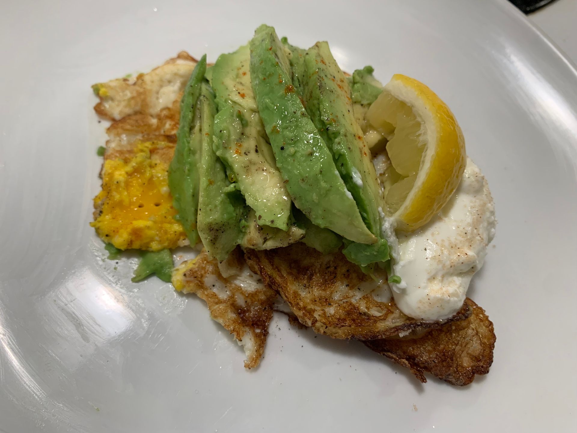 Fish taco with avocado slices, sour cream, lemon wedge, and yellow rice on a white plate