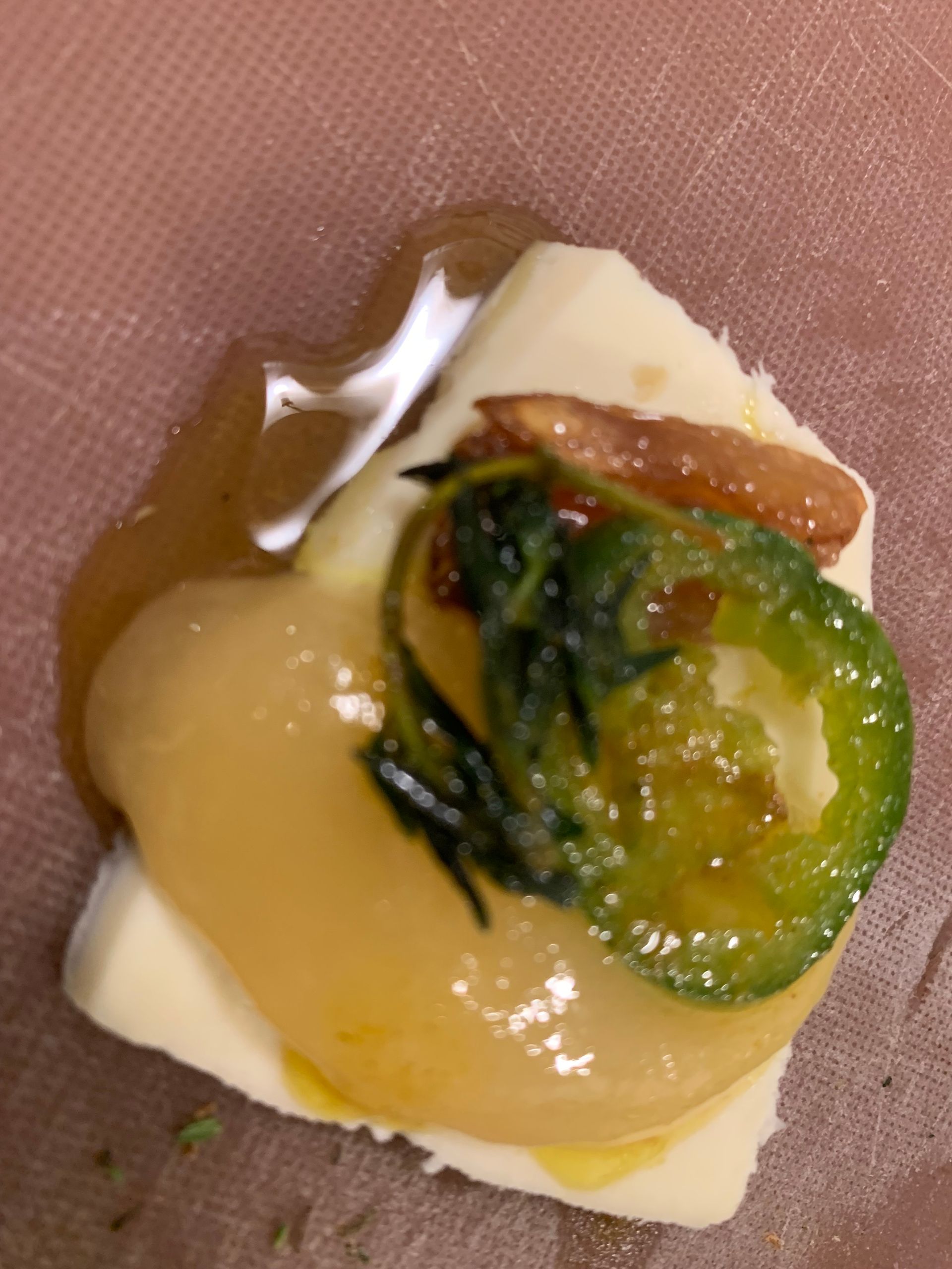 Small appetizer on a square cracker with melted cheese, green relish, and glossy sauce on a pink plate