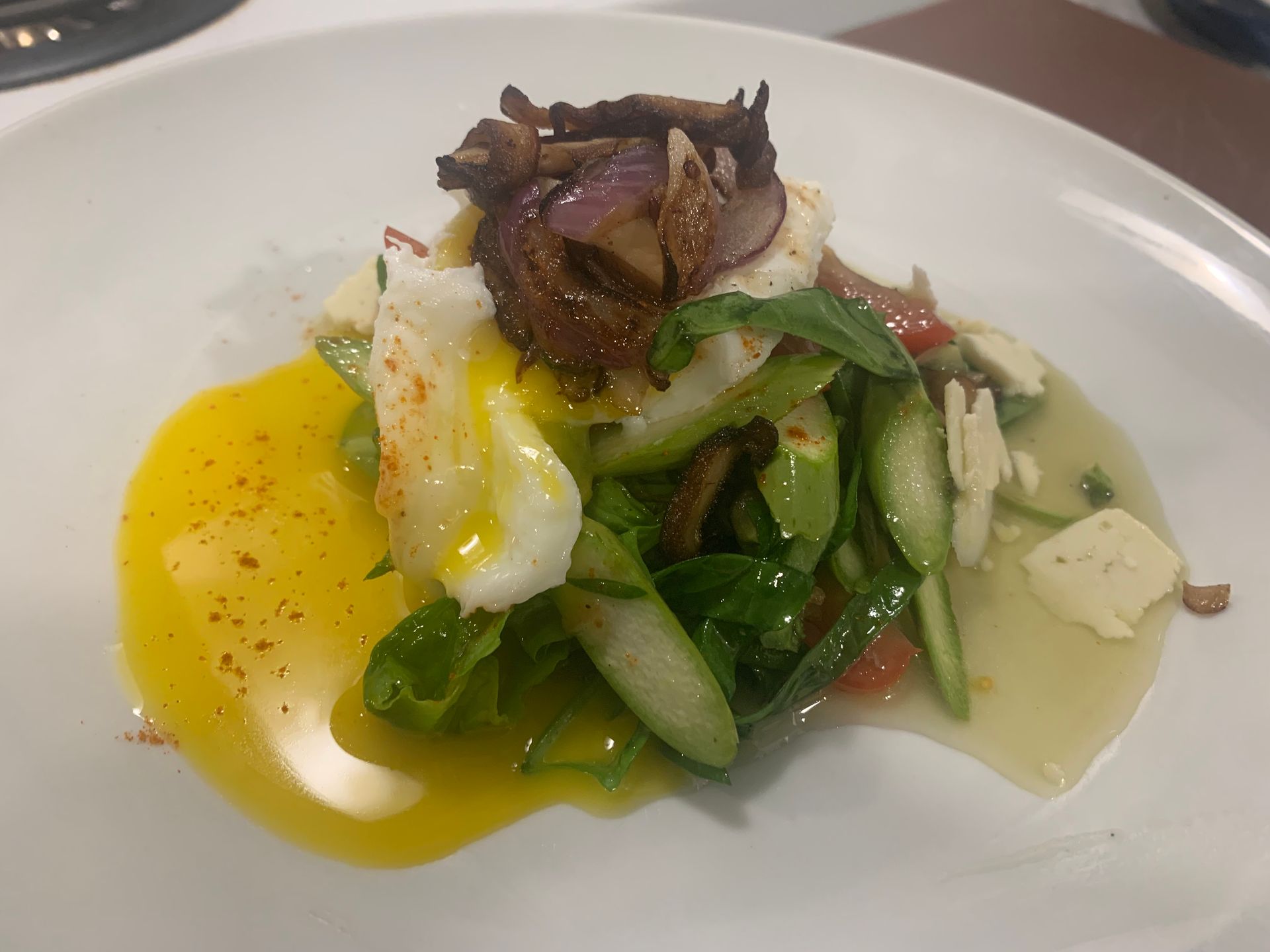 Plated gourmet salad with greens, mushrooms, and a bright yellow sauce on a white dish