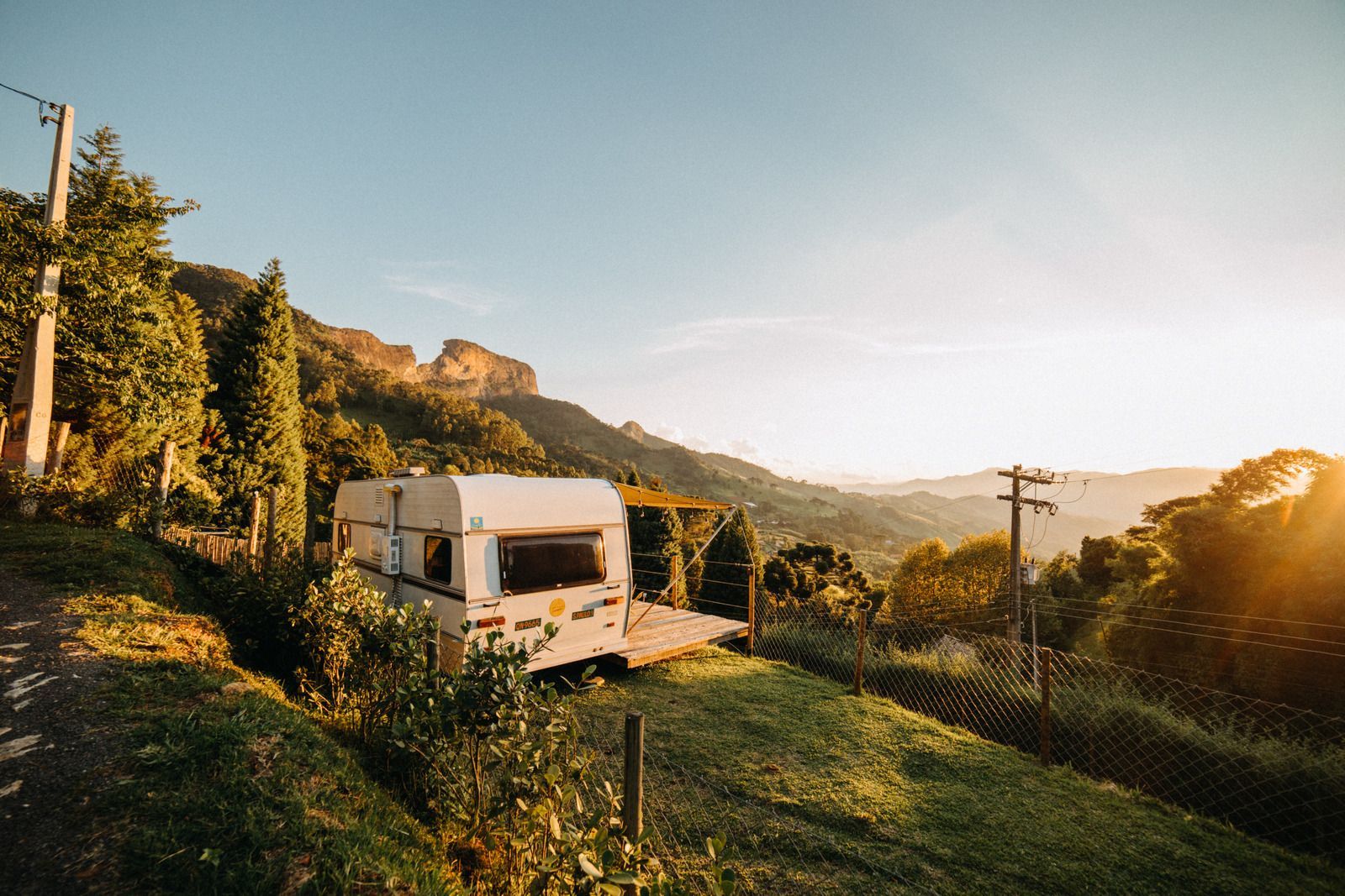 White camper van on a grassy hillside at sunset with mountains and trees in the background