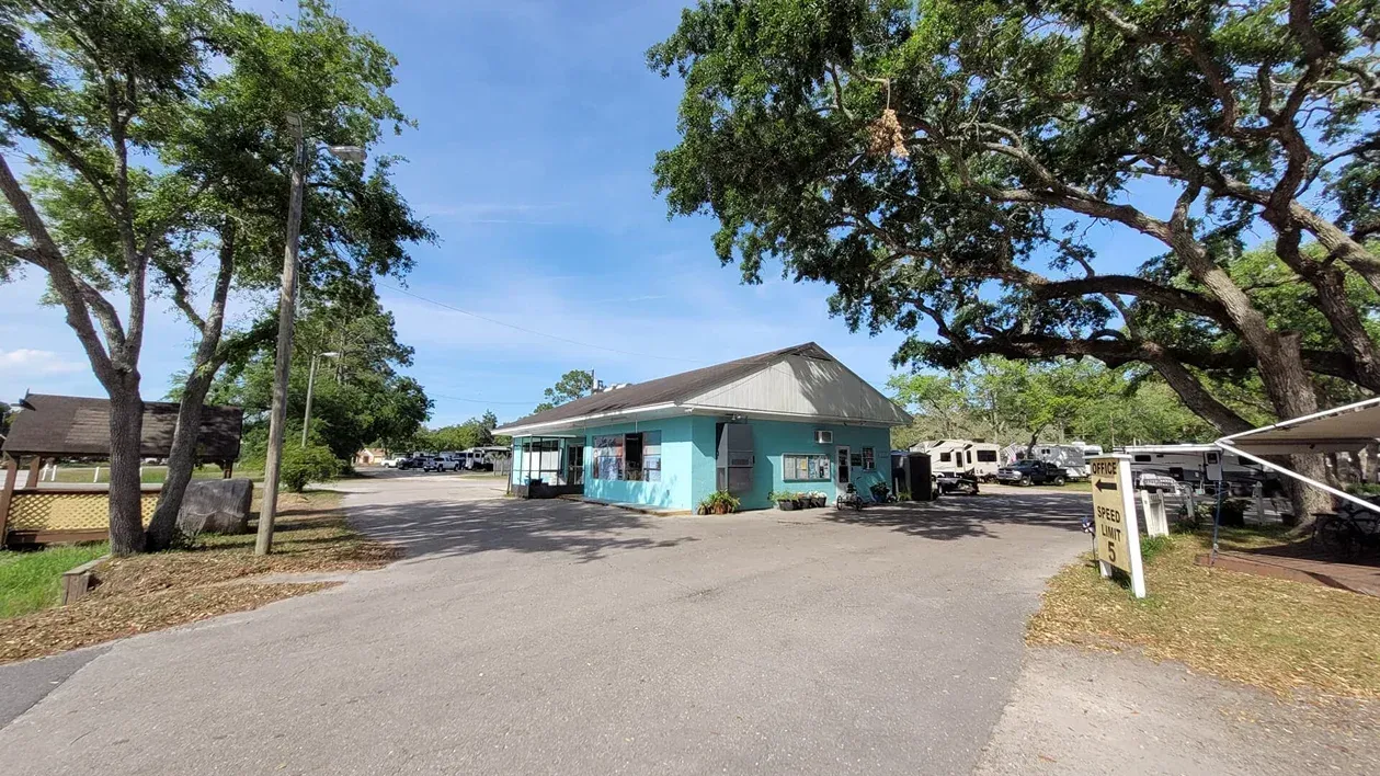 Small turquoise building beside a parking lot with trees and a clear blue sky