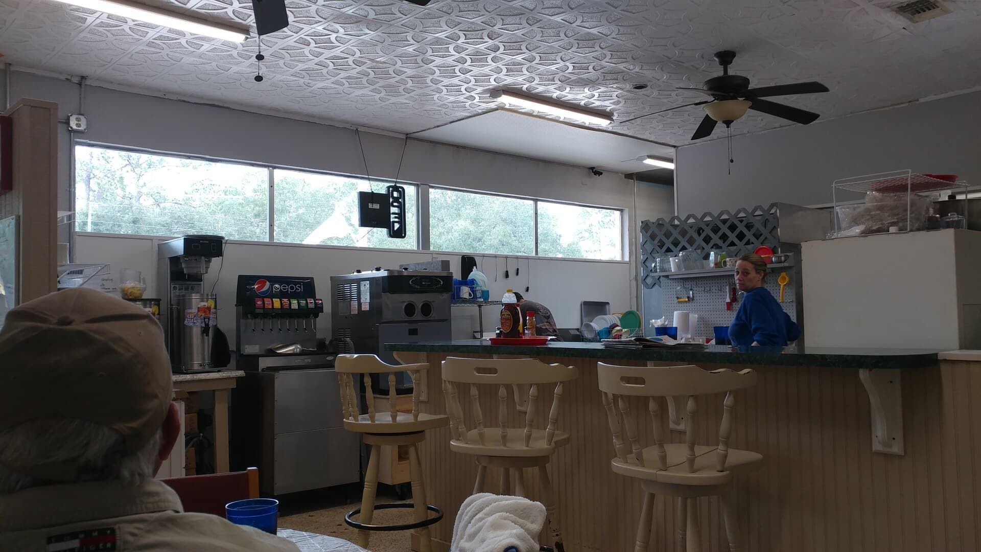 Kitchen with a bar counter, stools, coffee station, and ceiling fans under a windowed wall