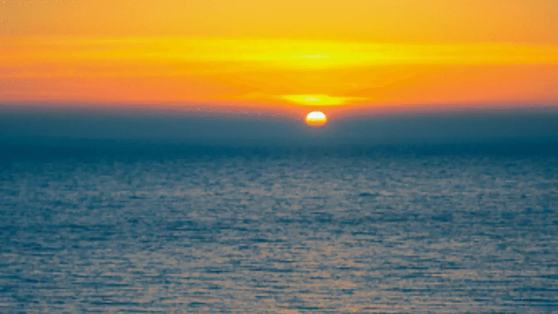 Sun setting over a calm blue ocean, with orange and yellow light across the horizon