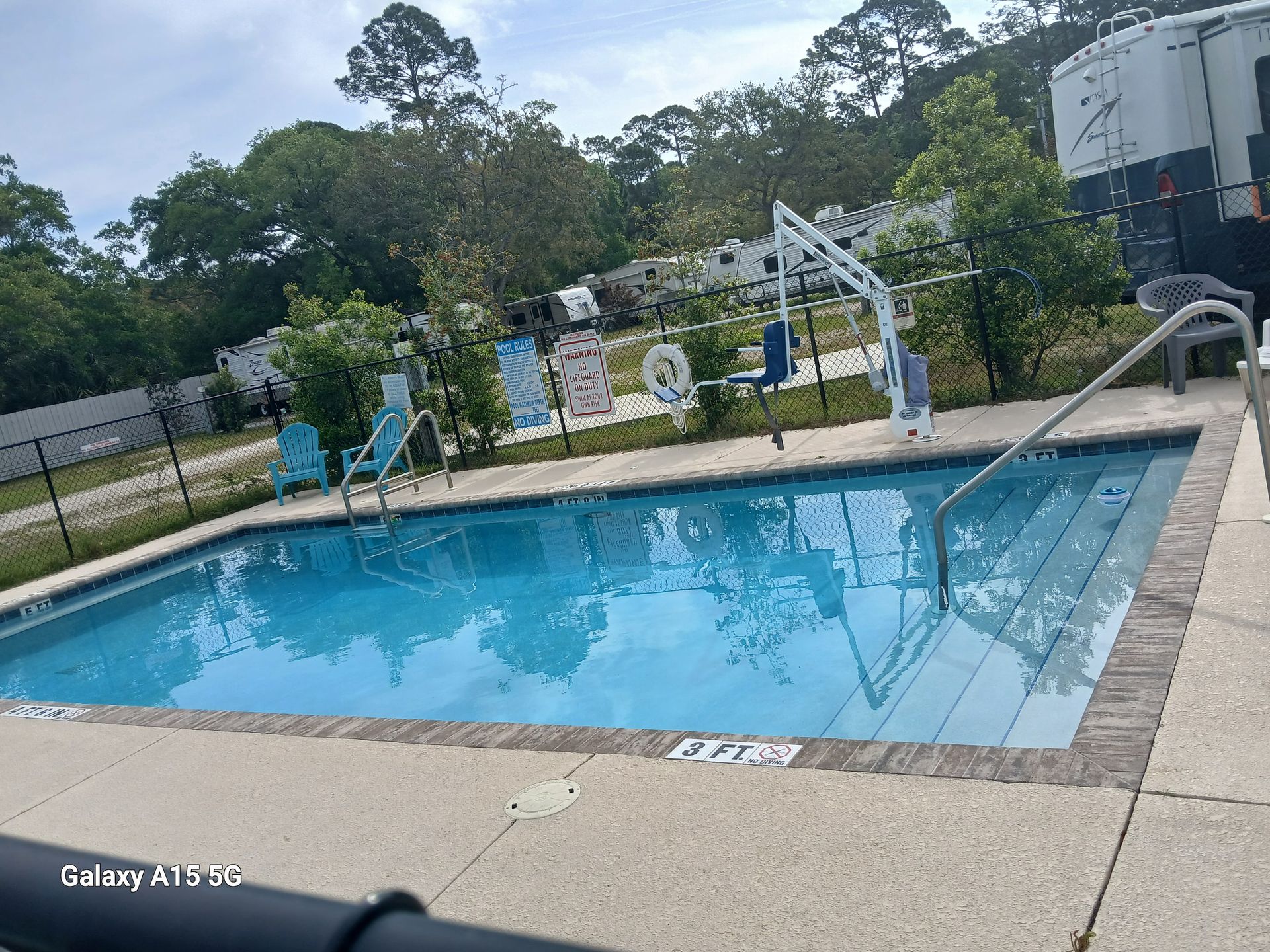 Outdoor swimming pool with diving board, lounge chairs, and trees in the background