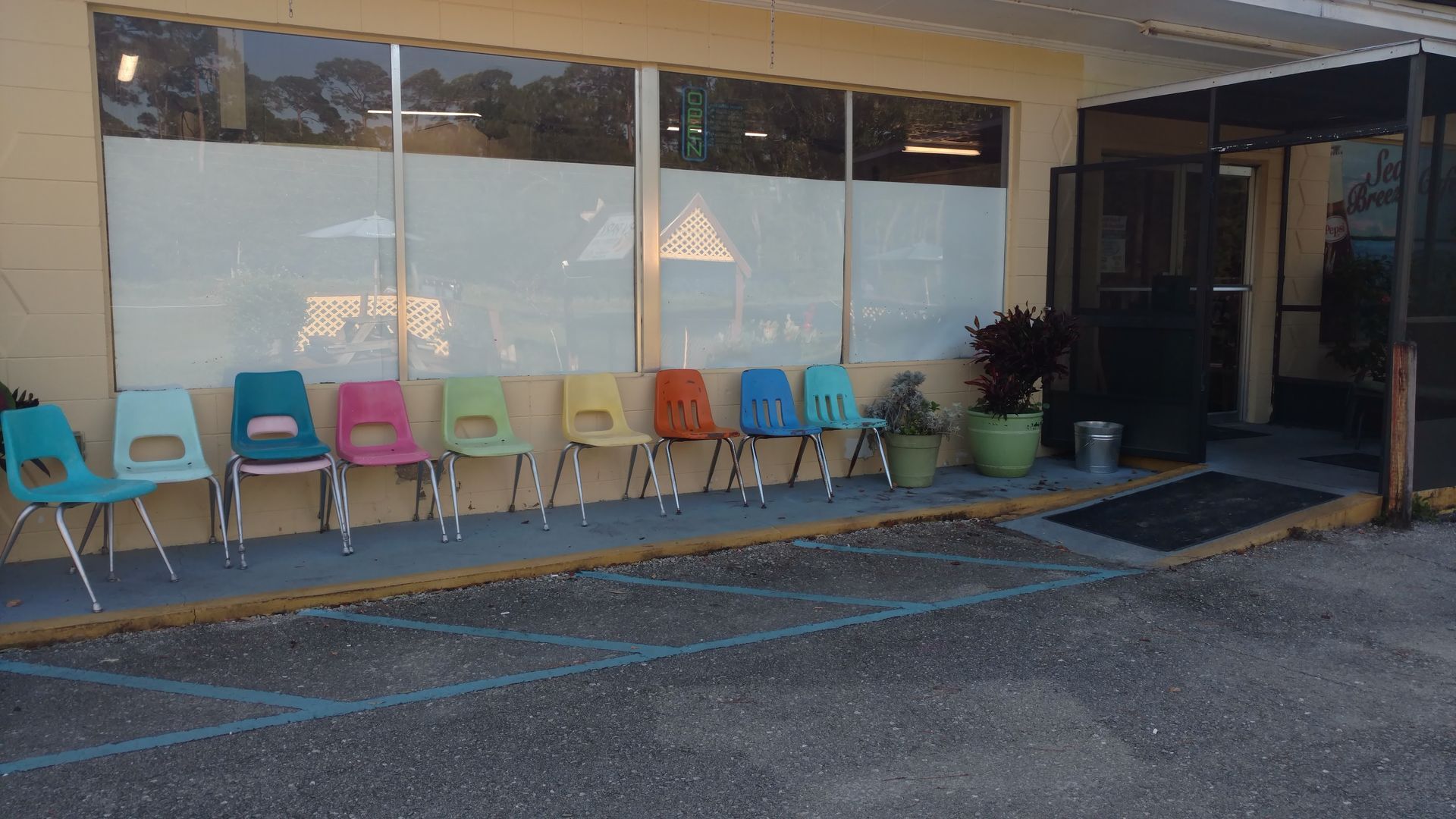 Colorful chairs lined up outside a storefront with large windows and a potted plant