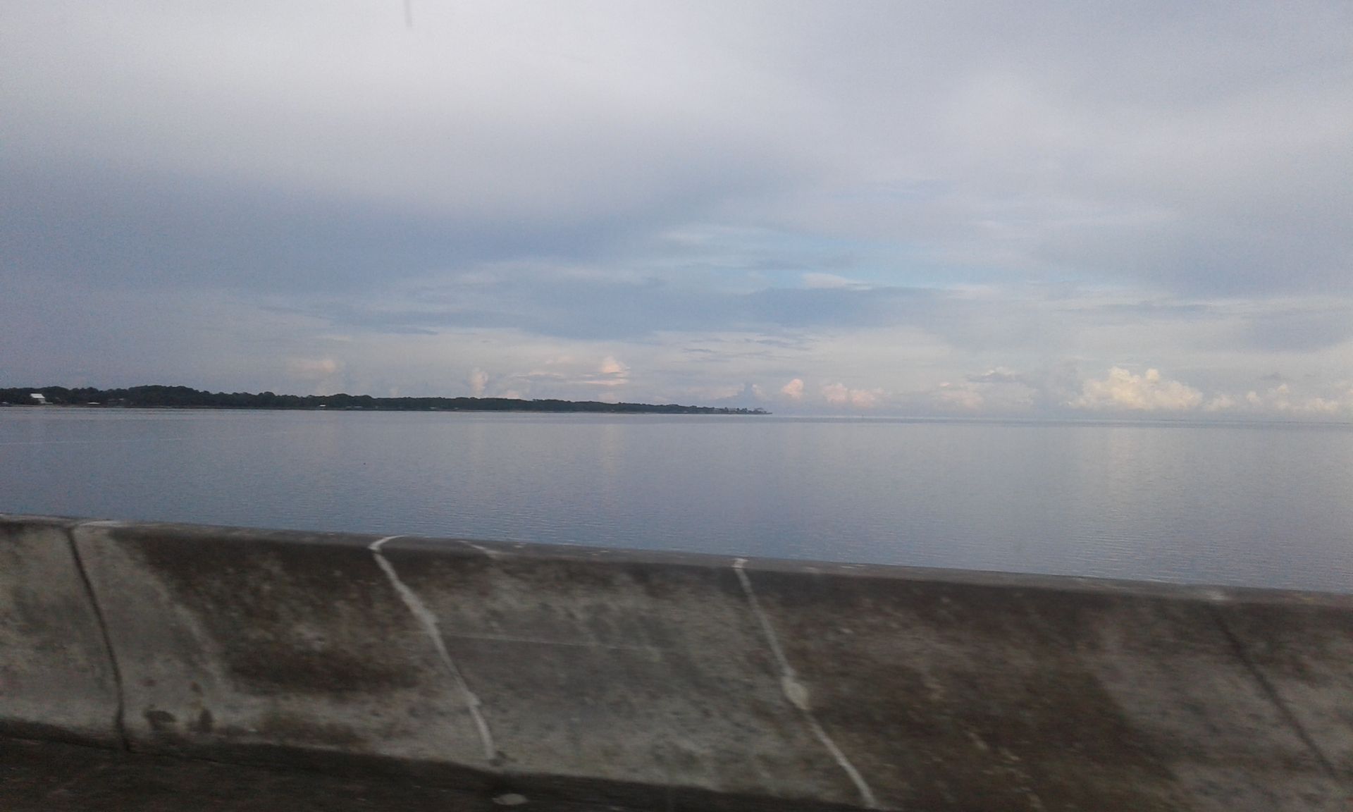 Calm gray sea under an overcast sky, viewed past a concrete seawall at the shore.