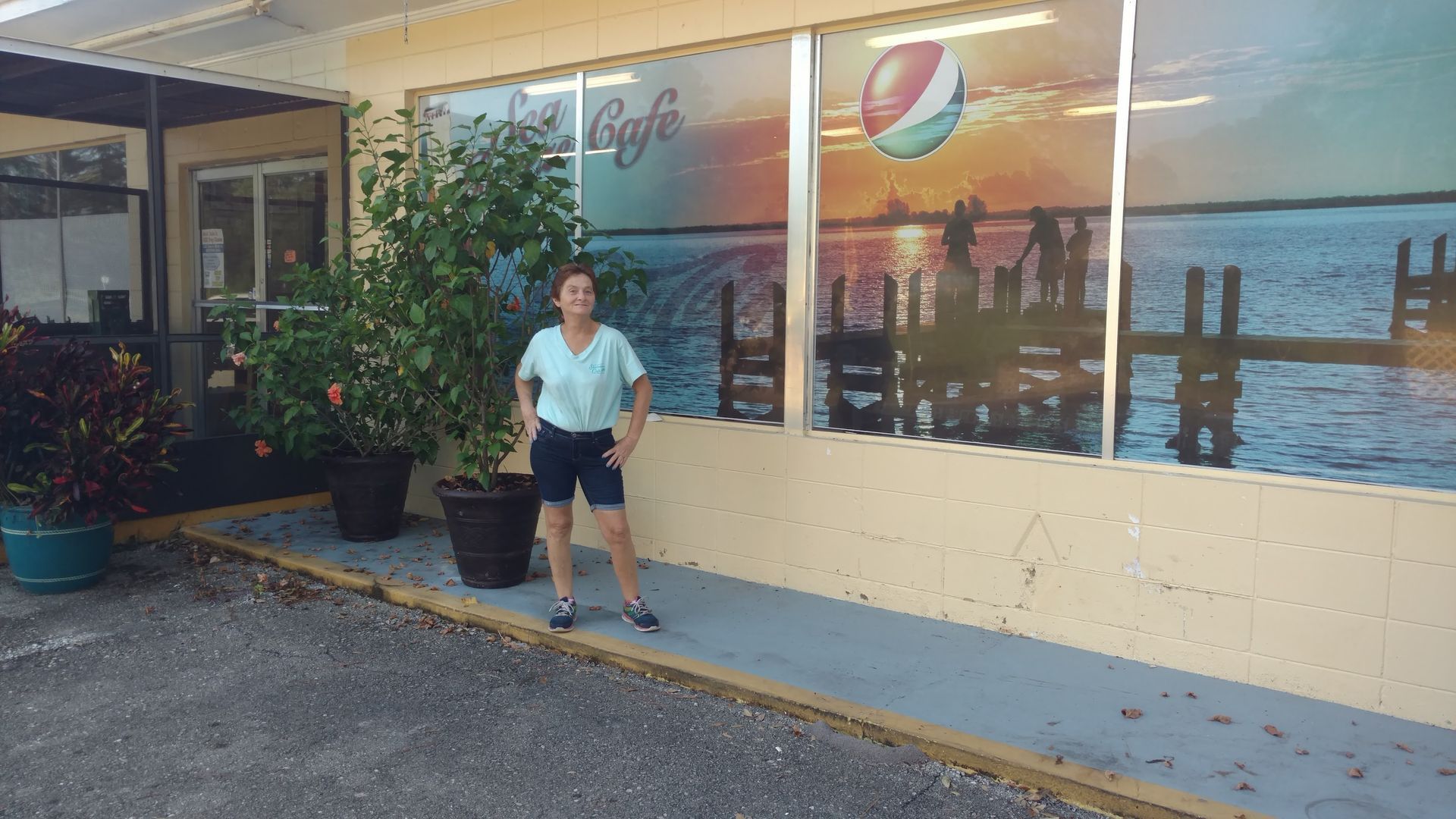 Person standing outside a café with a colorful mural and potted plants along the wall