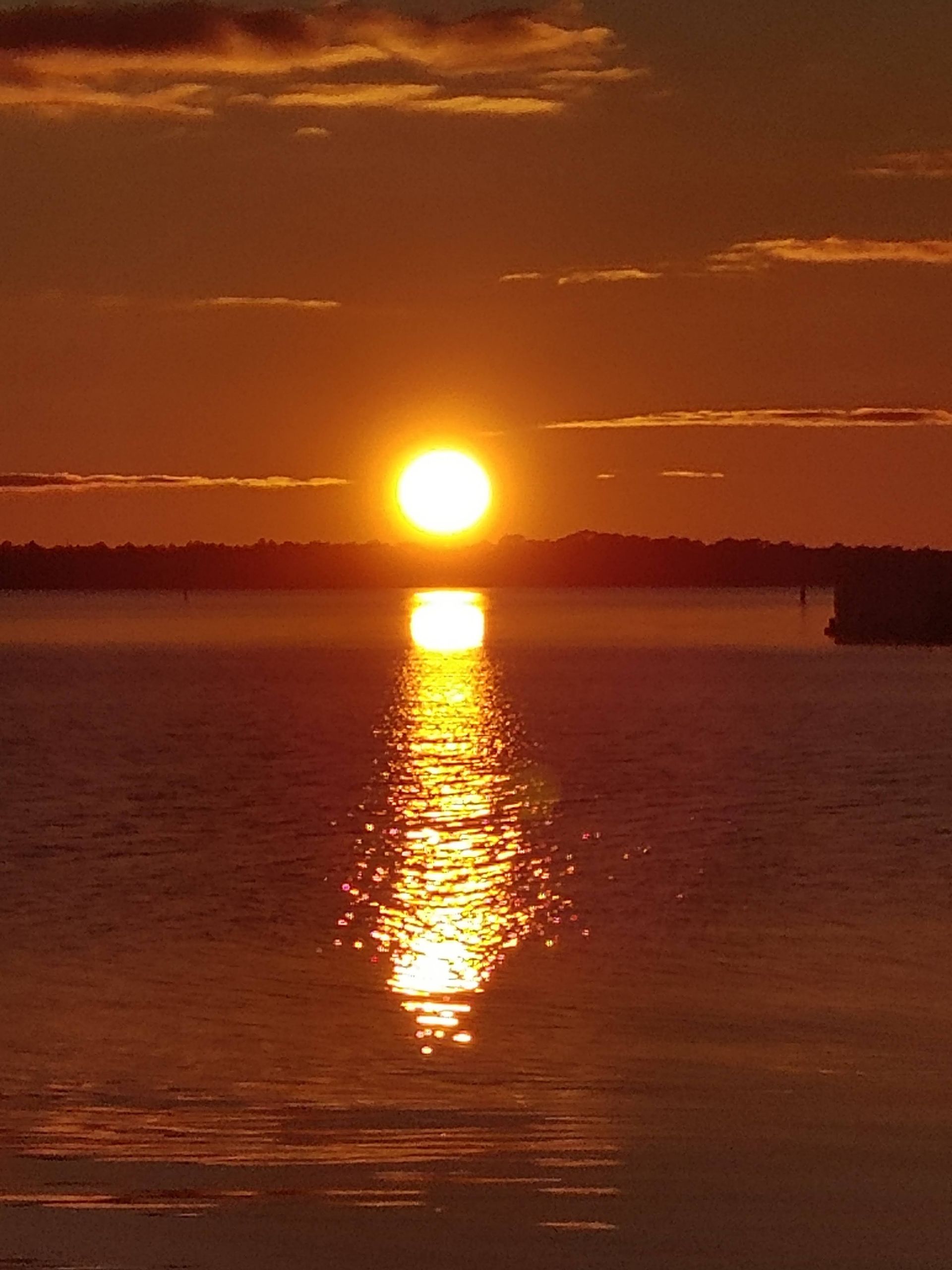 Sun setting over calm water, casting a golden reflection beneath an orange sky.