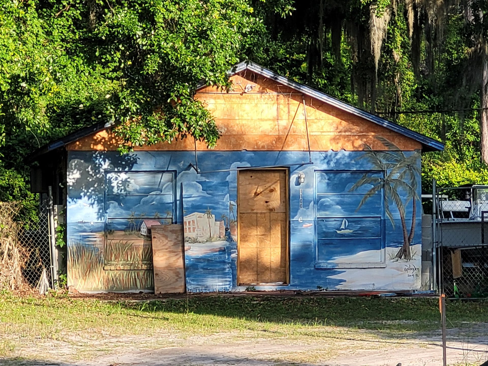 Small blue-painted wooden cabin with a tan door, set in a wooded area with sunlight and shadows.