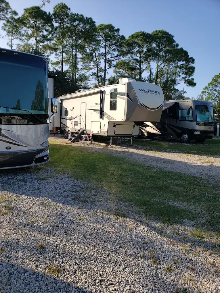 RVs parked on a gravel lot with trees in the background at sunset