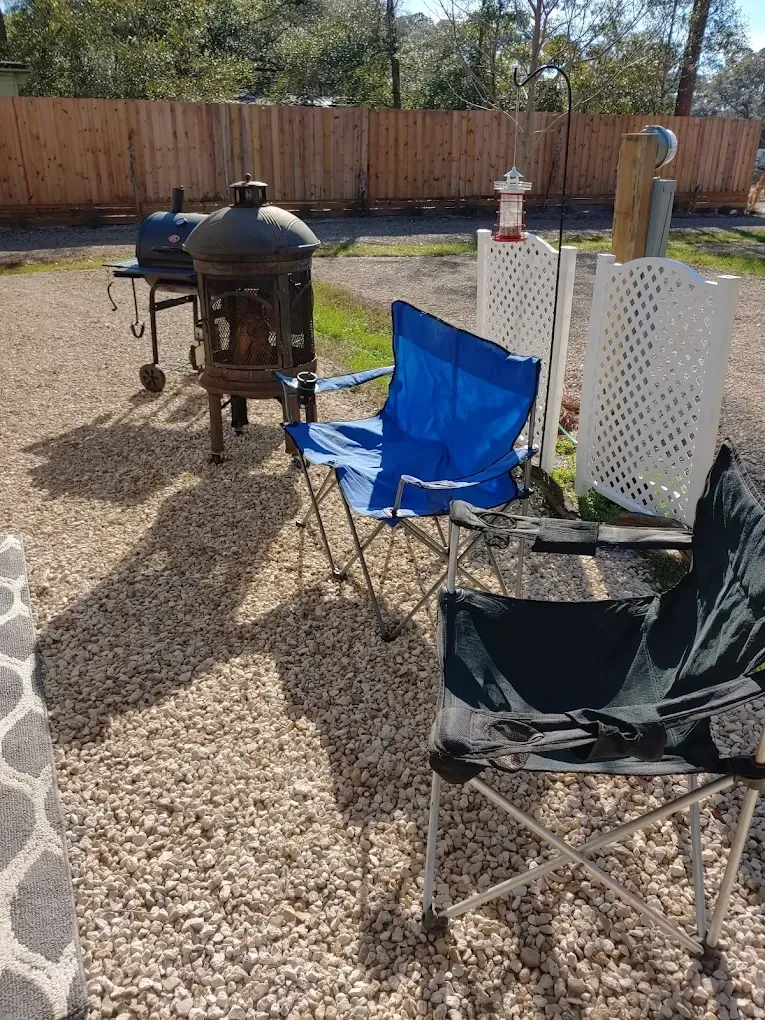 Backyard patio with folding chairs and a black smoker grill on a gravel ground.