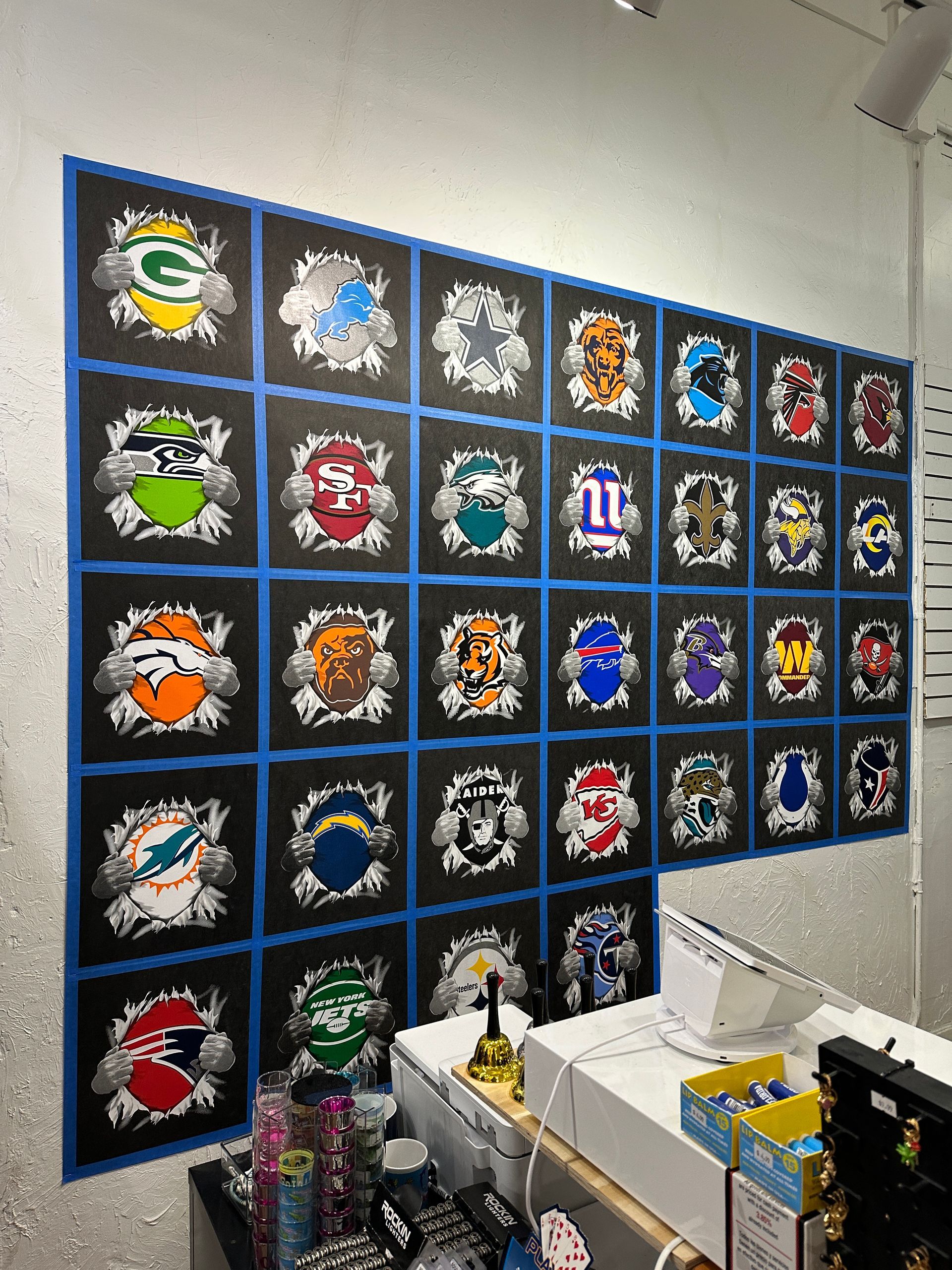 Wall display of 32 NFL team logos on black squares, with blue borders and a ripped effect.