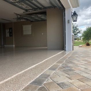 A garage with a brick driveway and a garage door open.