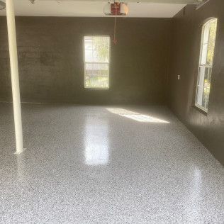 A large empty room with a gray floor and two windows.