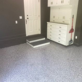 A garage with a door , stairs , cabinets and a broom.