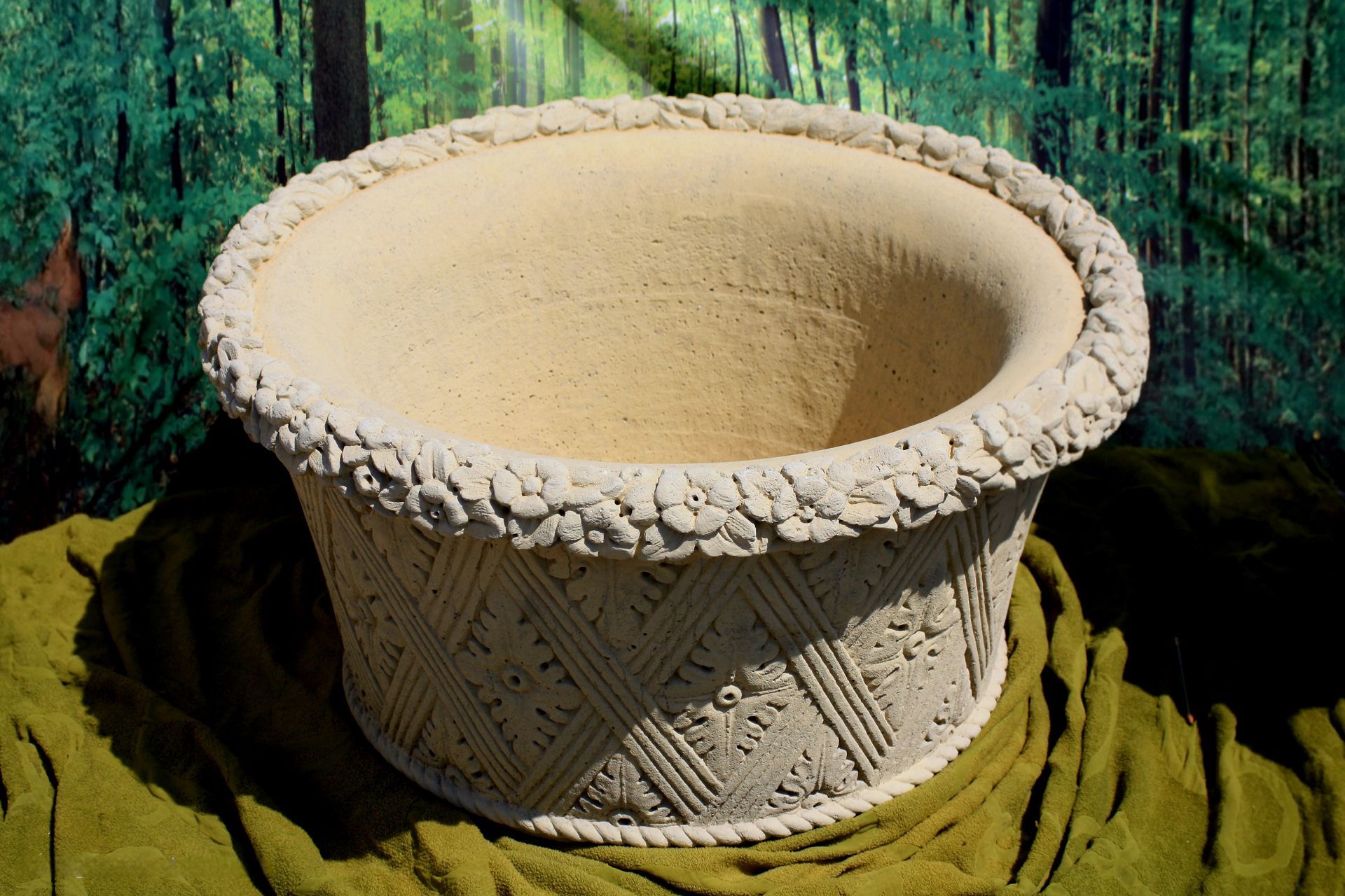 Rilievo di una fontana in pietra chiara con un volto di leone che zampilla acqua su uno sfondo di ciottoli.