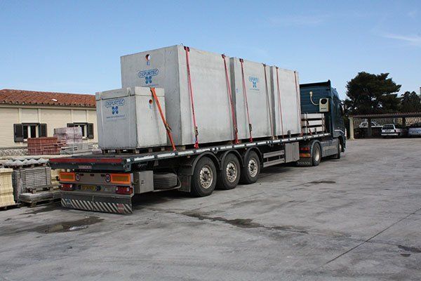 Autocarro a pianale ribassato che trasporta container imballati in un piazzale industriale.